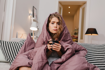 sad woman sitting on couch wrapped in blanket and holding a mug